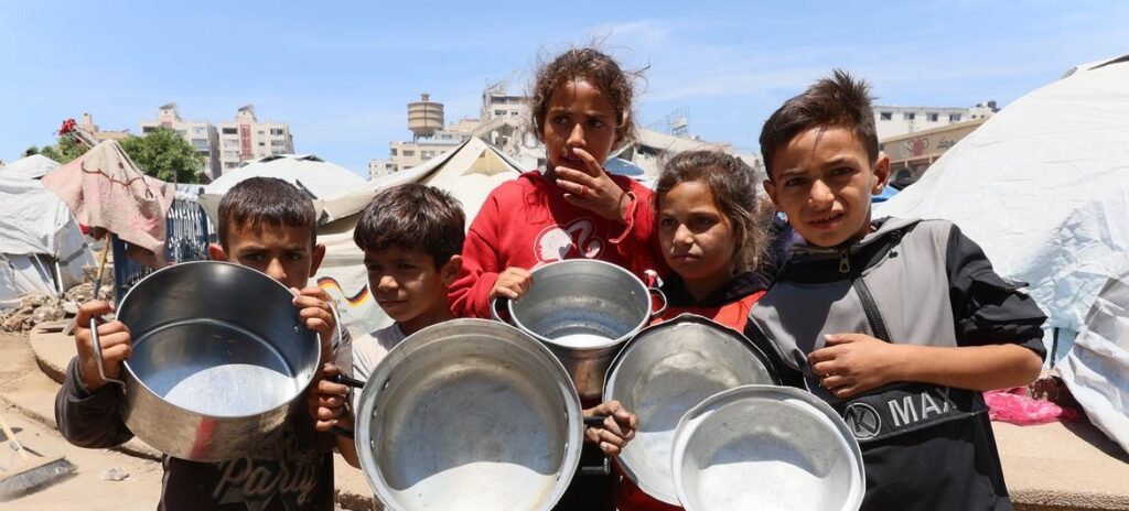 Imagen Noticias ONU   Niños en Gaza esperando a que les llenen los contenedores vacíos de comida.