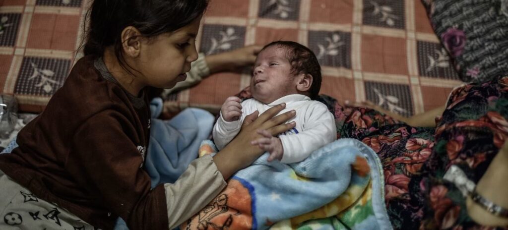 IMAGEN © UNICEF_Abed Zaqout Una niña cuida de su hermana pequeña en un refugio de Khan Younis