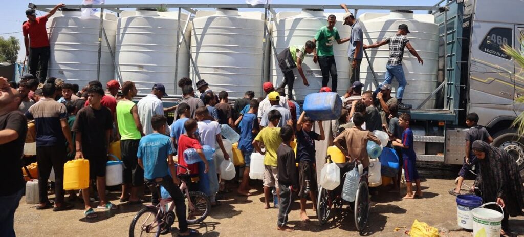 Imagen © UNICEF_Eyad El Baba Niños y sus familias recogen agua de un depósito de agua apoyado por UNICEF en Deir Al-Balah, en la Franja de Gaza.